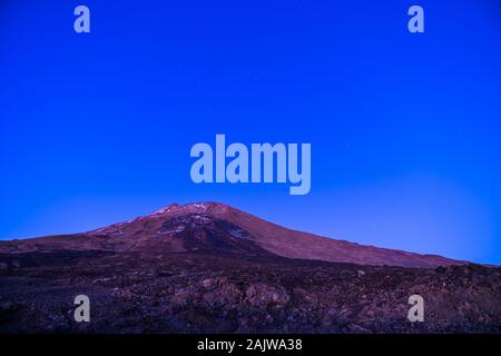 Spain, Tenerife, Starry sky and moonlight shining on snowy peak of volcano mountain teide late in the night Stock Photo