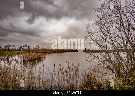 A view over a calm still lake captured on a dull, grey and overcast winter's day Stock Photo