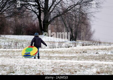 Child having fun on snow tube in a park, boy sliding down the hill. Winter entertainment, sledding in frosty day Stock Photo