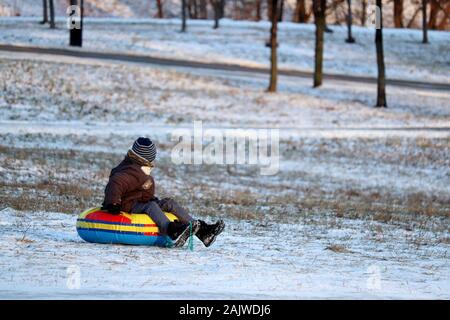 Child having fun on snow tube in a park, boy sliding down the hill. Winter entertainment, sledding in frosty day Stock Photo