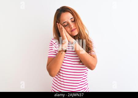 Young redhead woman wearing striped casual t-shirt stading over white isolated background sleeping tired dreaming and posing with hands together while Stock Photo