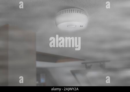 Domestic smoke alarm / battery powered smoke detector on the ceiling in room filled with smoke from fire at home Stock Photo