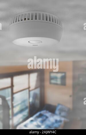 Domestic smoke alarm / battery powered smoke detector on the ceiling in room filled with smoke from fire at home Stock Photo