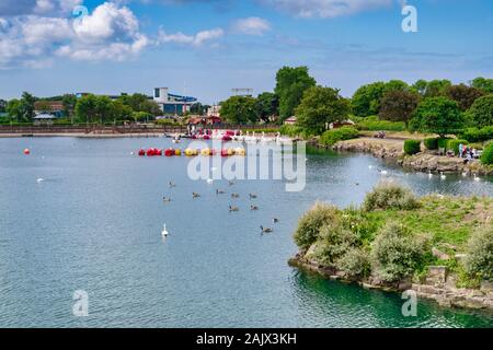 14 July 2019: Southport, Merseyside, UK - Marine Lake, the boating lake, with geese and swans, pleasure boats, holidaymakers walking around in the sun Stock Photo