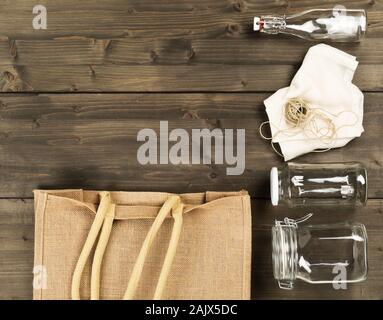 Zero waste or waste free shopping utensils with burlap bag, glass bottles and cotton bag on brown wooden table background flat lay from above - waste Stock Photo