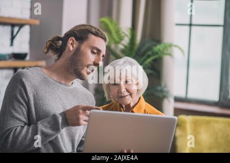 Grey-haired mom and her son discussing online shopping variants Stock Photo