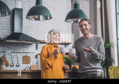 Young handsome man in grey shirt and his mom talking in the kitchen Stock Photo