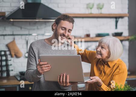 Grey-haired mom touching her sons cheek and smiling Stock Photo