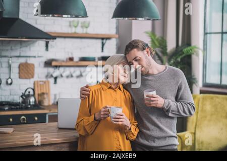 Young handsome man in grey shirt and his mom feeling great together Stock Photo