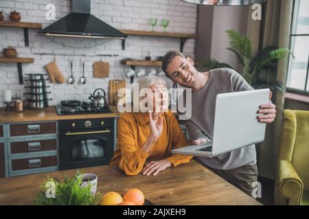 Young handsome man in grey shirt and his mom having video call with friends Stock Photo