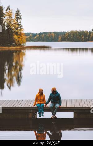 Couple friends traveling in Finland family lifestyle love relationship man and woman sitting talking on pier outdoor lake and autumn season forest lan Stock Photo