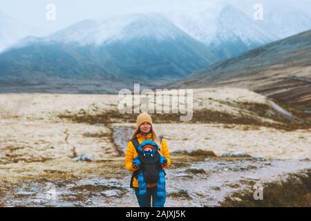 Mother traveling with baby carrier hiking family healthy lifestyle woman and child active vacations outdoor in Norway mountains Rondane park Stock Photo