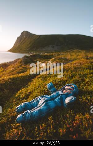 Baby traveler laying on moss relaxing with mountains and sea view family activity healthy lifestyle with kids vacations outdoor child wearing jumpsuit Stock Photo