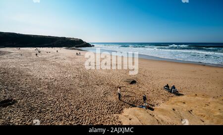 Sintra, Portugal - Jan 5, 2020: Families enjoy a relaxing afternoon at the golden Praia das Macas in Portugal on a sunny winter day Stock Photo