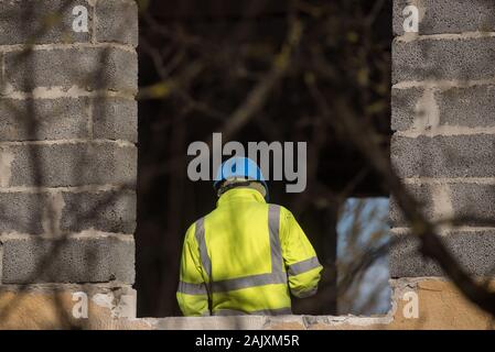 RIGA, LATVIA. 25th March 2019. Selective focus photo. Worker with blue plastic helmet on head and yellow reflecting vest works at building yard. Stock Photo