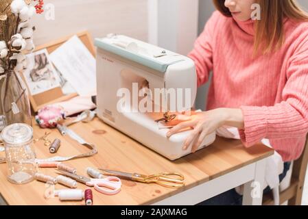 Seamstress works on a sewing machine. The girl sews and holds a pink cloth. Stock Photo