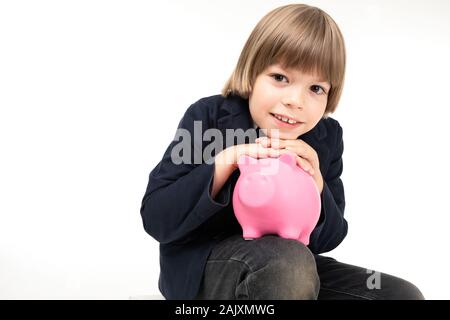 Pretty teenager boy in black costume sits with pink pig moneybox isolated on white background Stock Photo