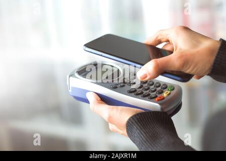 Customer hand pays with smartphone in store using NFC technology. Mobile phone paying the bill with contact less technology. Stock Photo