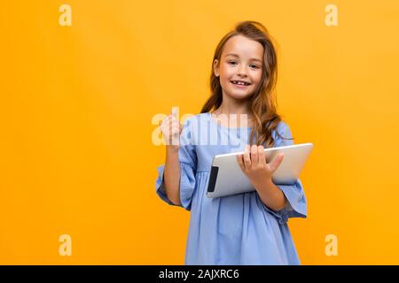 girl in a beautiful dress of delicate blue color with a tablet in hand on a yellow background with copy space