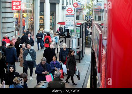 People shoppers wearing winter clothing standing waiting for a bus at a bus stop outside Uniqlo store in Oxford Street London England UK  KATHY DEWITT Stock Photo