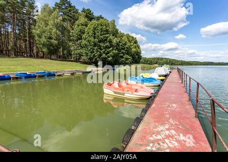 colored old vintage plastic catamarans and boats near a metal pier on the sand shore of a large lake Stock Photo