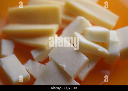 Two kinds of hard cheese on a plate close-up, rectangular slices of maasdam and cheddar. Stock Photo