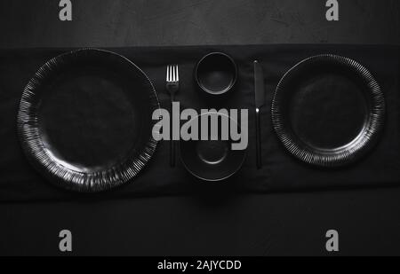 Black tableware, plates, bowls and cutlery, empty dishes, on black table. Flat lay of empty dishes. All black tableware. Dinner settings. Empty plates Stock Photo