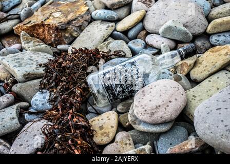 Washed up glass bottle and seaweed on english pebble beach Stock Photo