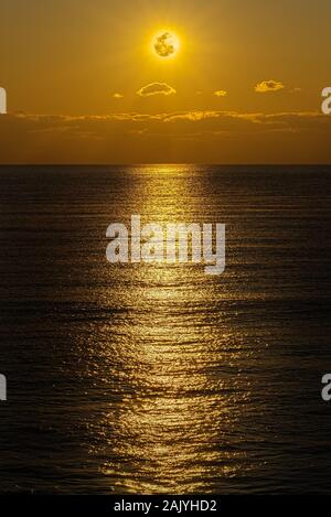 The moon and clouds in the golden sky above the ocean horizon at midnight, moonlight is reflected in the ribbed surface of the water. Night landscape, Stock Photo