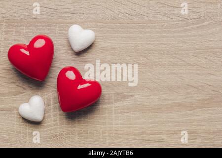 Stock photo of two red plastic hearts and two white hearts on a wooden background. Hearts on the left side with space for text Stock Photo