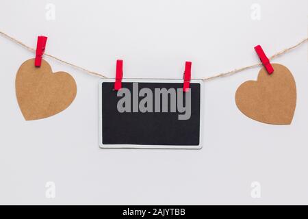 Stock photo of two paper hearts and a blackboard hanging on a rope with red clothespins on a white background Stock Photo