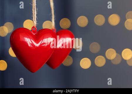 Stock photo of two red plastic hearts hanging on a bluish background and unfocused lights. Hearts on the left side with space for text Stock Photo