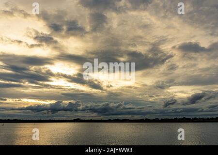 The clouds filled the sky, obscuring the light from the sun during the sunset. The sky on the top is coloured orange from the sun. The bottom sky is b Stock Photo
