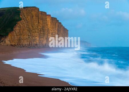 West Bay, Dorset, UK.  6th January 2020. UK Weather.  Rough seas crash ashore on East Beach at West Bay in Dorset as the light fades at dusk looking towards the famous cliffs which featured in ITV’s Broadchurch.  Picture Credit: Graham Hunt/Alamy Live News Stock Photo