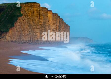 West Bay, Dorset, UK.  6th January 2020. UK Weather.  Rough seas crash ashore on East Beach at West Bay in Dorset as the light fades at dusk looking towards the famous cliffs which featured in ITV’s Broadchurch.  Picture Credit: Graham Hunt/Alamy Live News Stock Photo