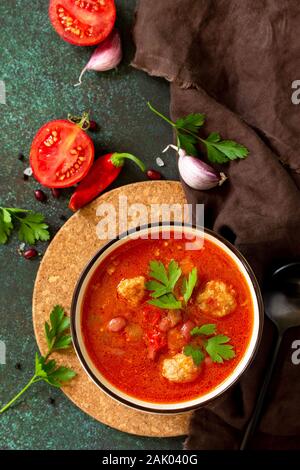 Tomato soup with meatballs and chili peppers on a dark stone or slate table. Stock Photo