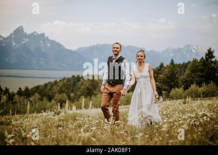 Bride and Groom walk through wildflowers in front of Teton mountains Stock Photo