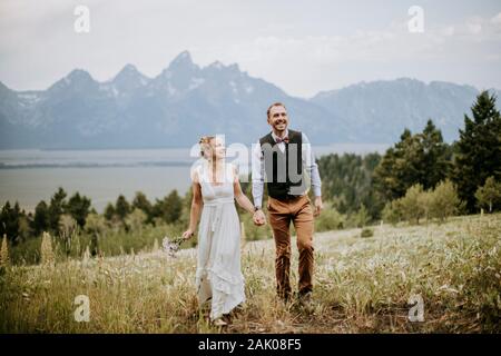 Newlywed bride and groom walk through field in Grand Teton Park. Stock Photo