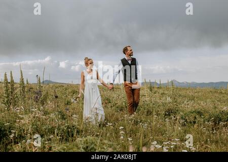 Bride and groom walk through field of wildflowers in Wyoming Stock Photo