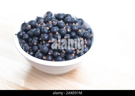 white bowl filled with black currant berries, on table, white background Stock Photo