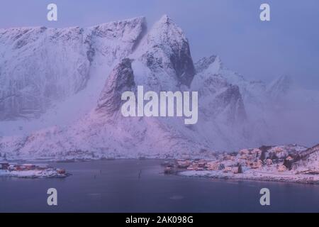 Mountain peaks rise over coastal village of Reine in winter twilight, Moskenesøy, Lofoten Islands, Norway Stock Photo