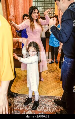 Dilijan, Armenia, January 01, 2019: A Little offended girl in a white dress dances with relatives on new year's eve in the dining room of the 'Mountai Stock Photo