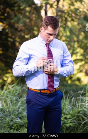 Young man in suit stands outside adjusting tie. Stock Photo