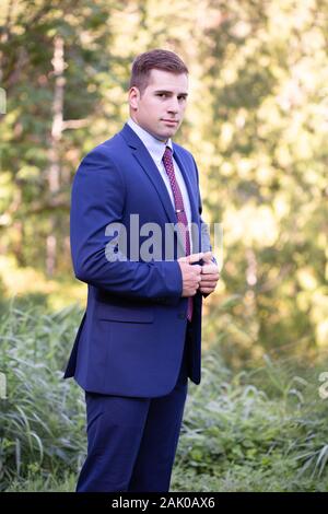 Confident young man in suit stands in front of trees. Stock Photo