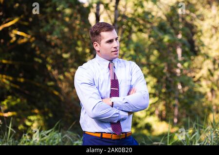 Young man in suit stands confidently outside with arms crossed. Stock Photo