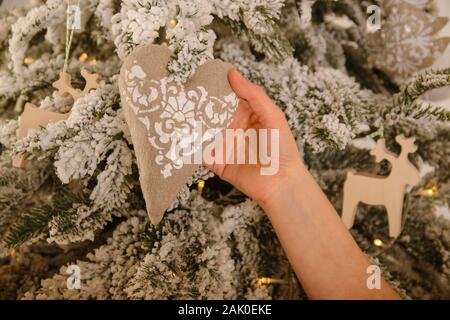 woman's hand holds a decoration for the Christmas tree in the shape of a heart from rough linen fabric of gray color Stock Photo