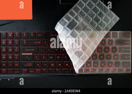 silicon dust keyboard cover folded and covering half of red glowing back lit keyboard of a gaming laptop. Stock Photo