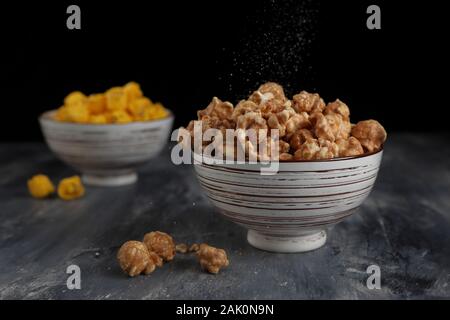 A close up of salt sprinkling over caramel popcorn in a bowl taken in the studio.