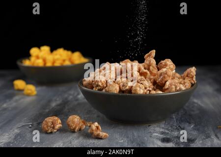 A close up of salt sprinkling over caramel popcorn in a shallow green bowl taken in the studio. Stock Photo