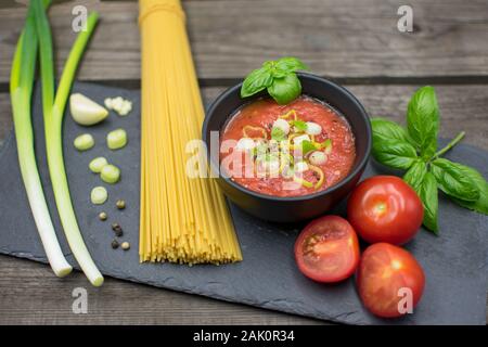 fruity tomato sauce in a bowl decorated with spring onions and basil. Served with raw spaghetti. Stock Photo